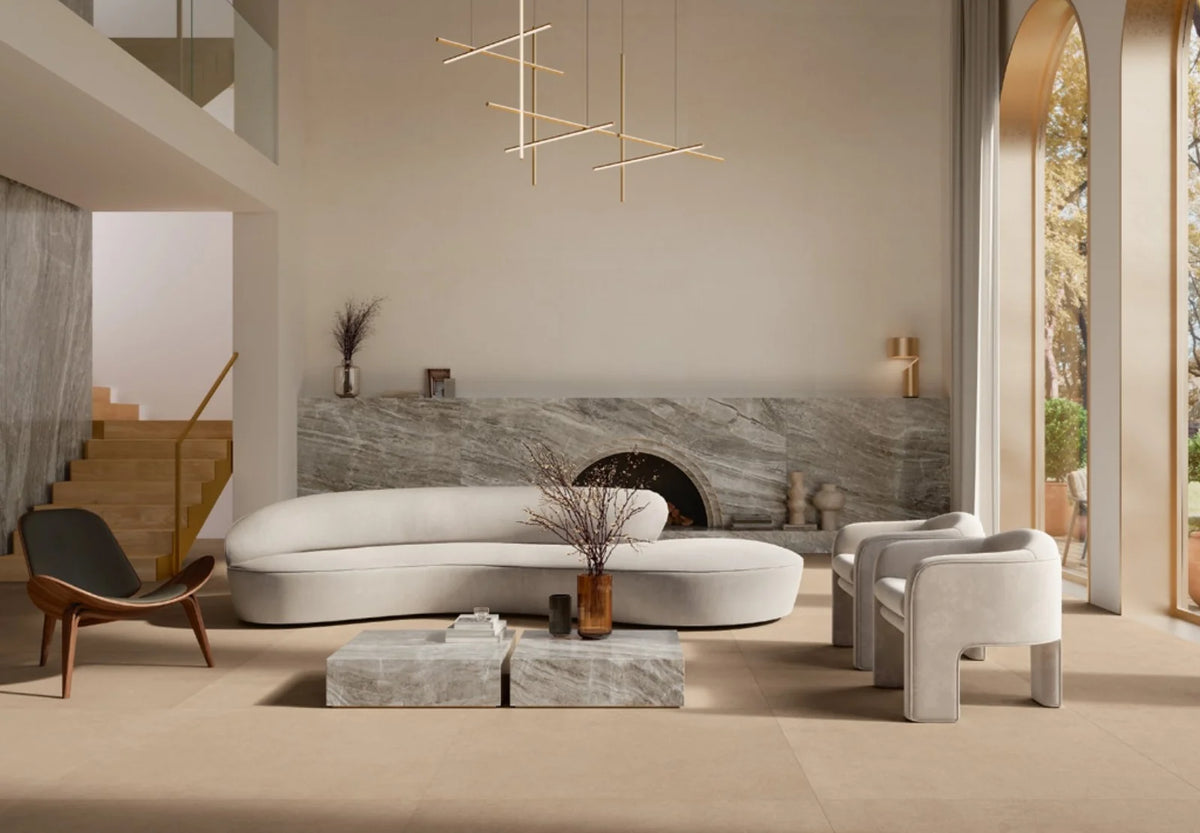 Balance Tan Matt 600x600mm floor tiles in a luxury open-plan living room featuring a curved white sofa, marble fireplace surround, and gold pendant lighting.