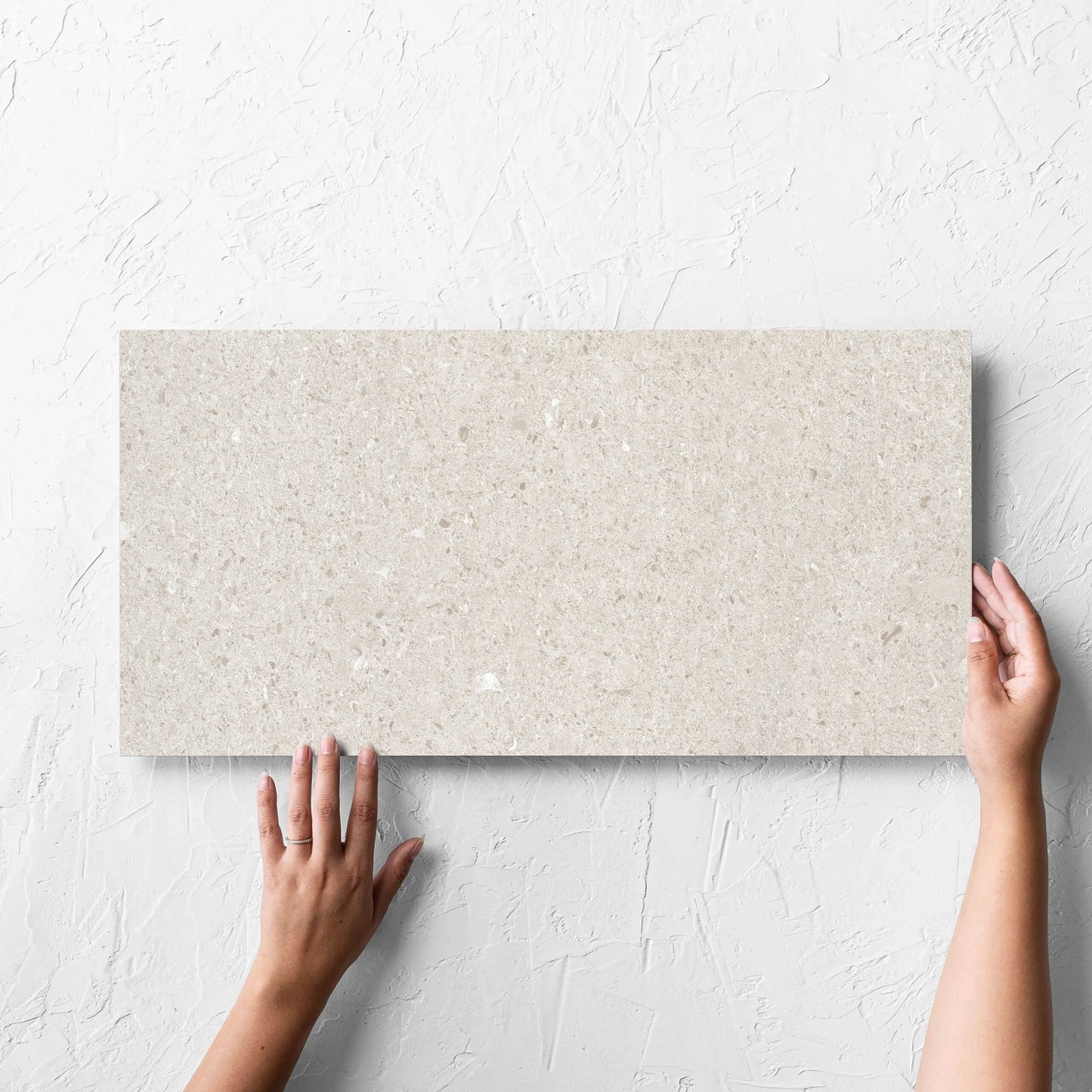 Hand holding a single Bayside Champagne Shell Matt 300x600mm tile against a white rendered wall, showing the matt surface