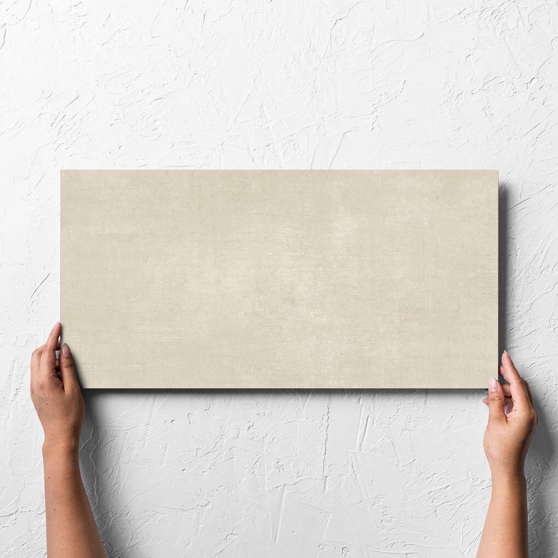Hand holding a single Bayside Sand Natural Matt 300x600mm tile against a white rendered wall, showing the matt surface