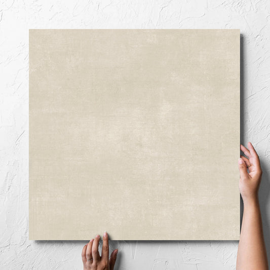 Hand holding a single Bayside Sand Natural Matt 600x600mm tile against a white rendered wall, showing the matt surface