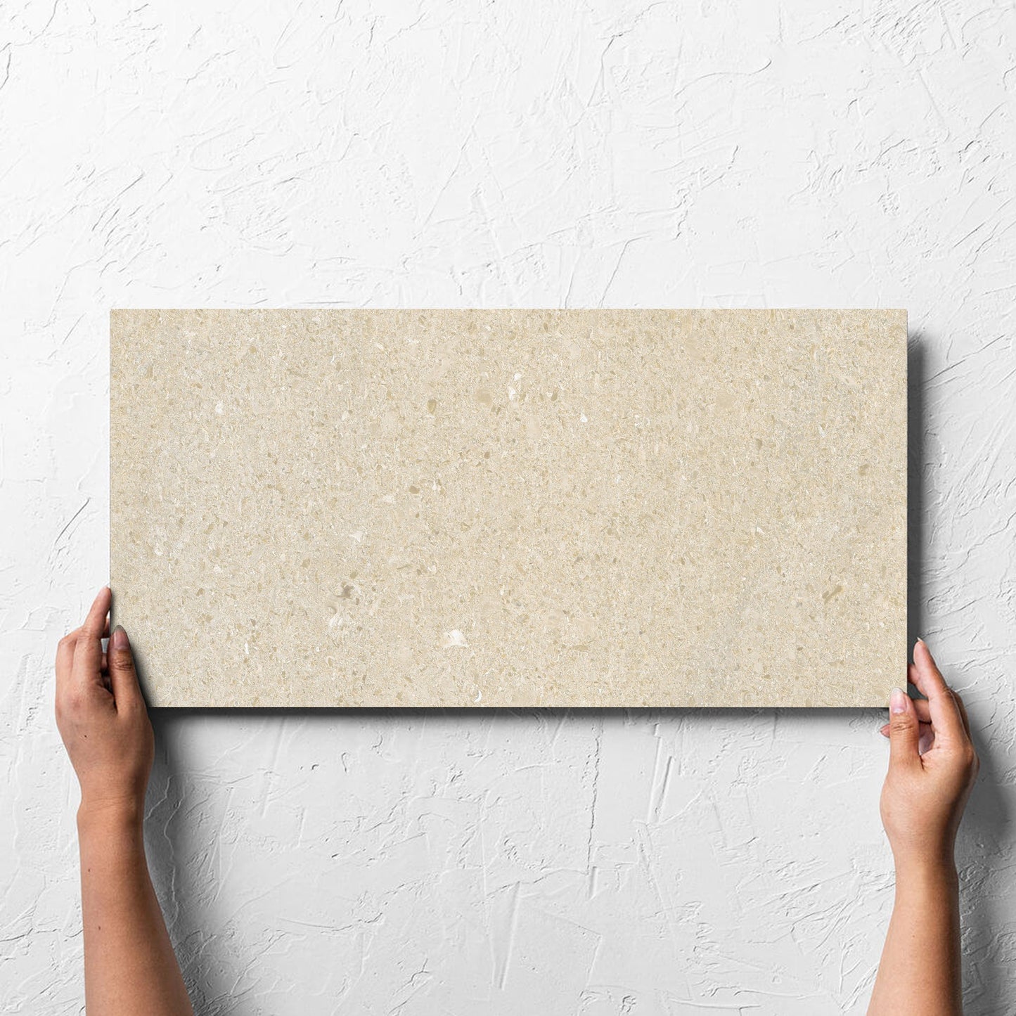 Hand holding a single Bayside Sand Shell Matt 300x600mm tile against a white rendered wall, showing the matt surface