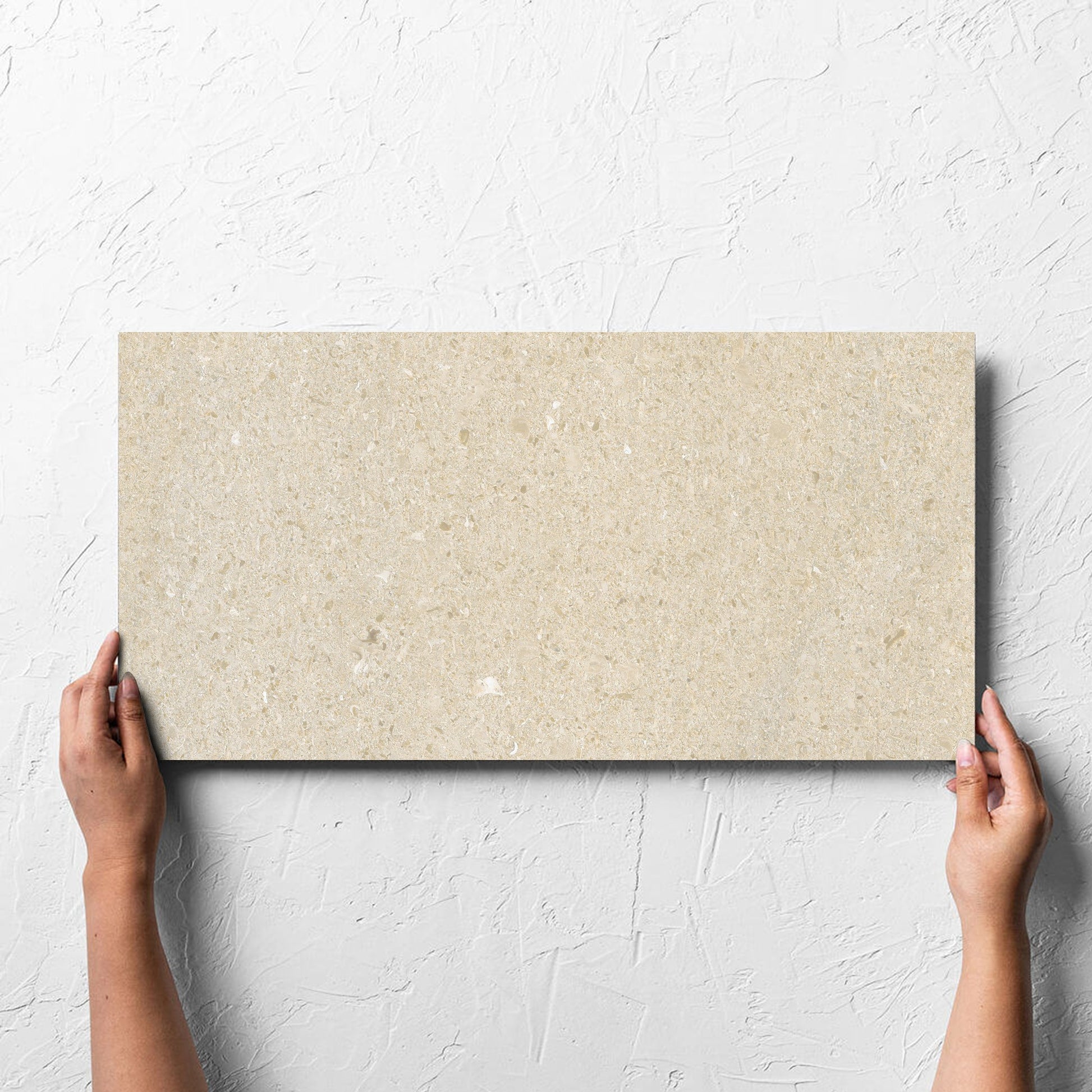 Hand holding a single Bayside Sand Shell Matt 300x600mm tile against a white rendered wall, showing the matt surface