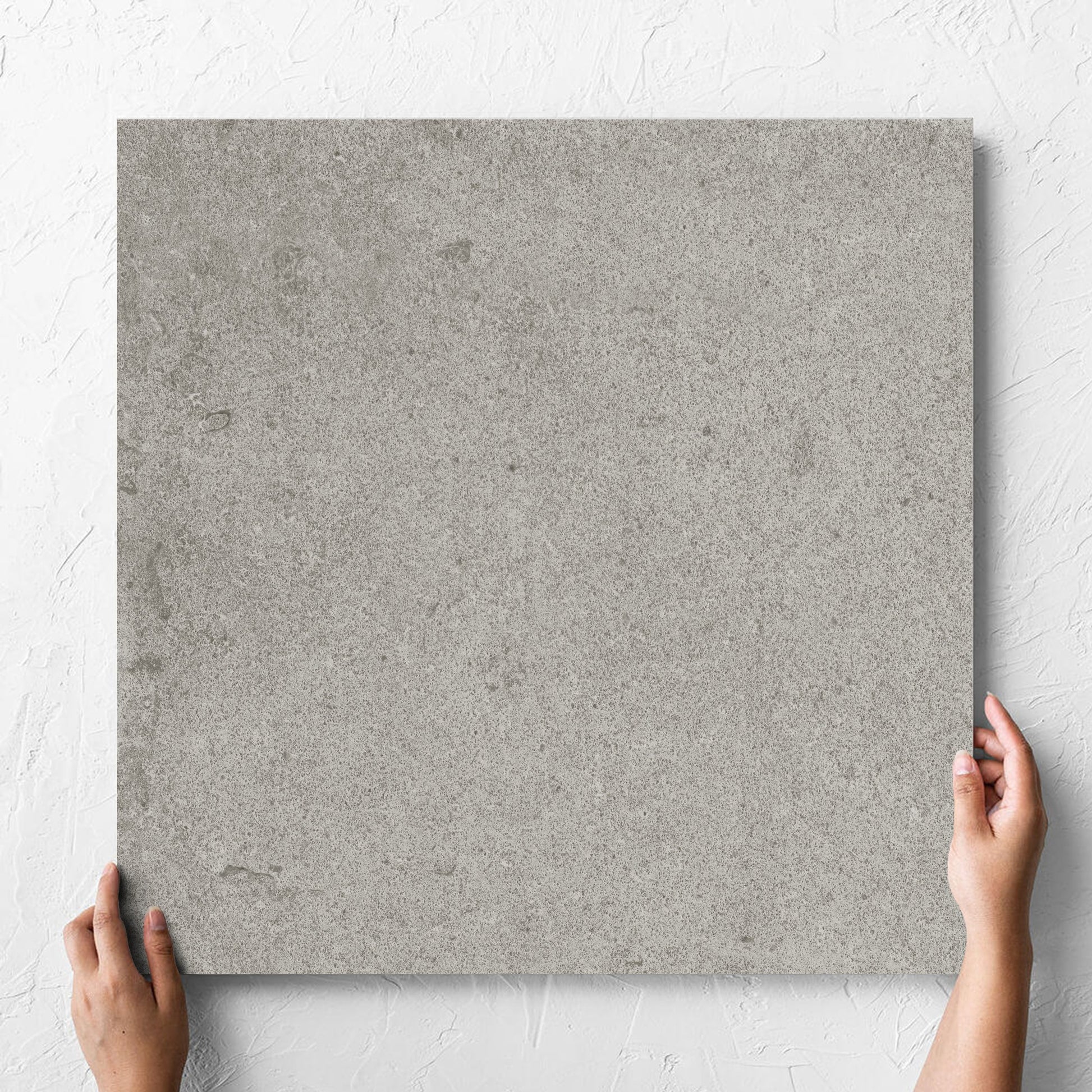 Hand holding a single Beachstone Grey Grip 600x600x20mm tile against a white rendered wall, showing the matt surface