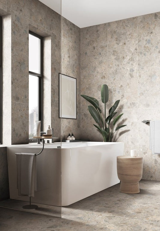 Bedrock Beige Matt 300x600mm tiles covering full-height bathroom walls beside a freestanding white bath, tall indoor plant, and natural stone side table.