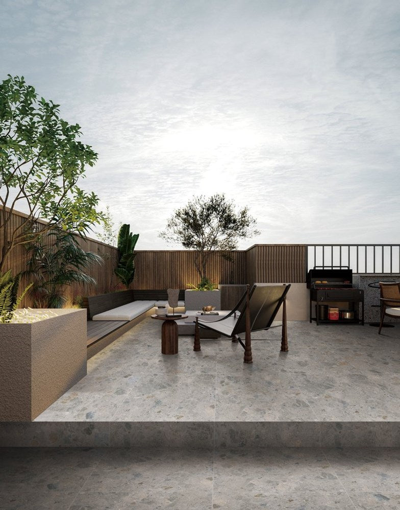 Bedrock Mid Grey Matt 600x600mm porcelain tiles laid on a contemporary rooftop terrace featuring outdoor lounge seating, a BBQ station, and potted trees.