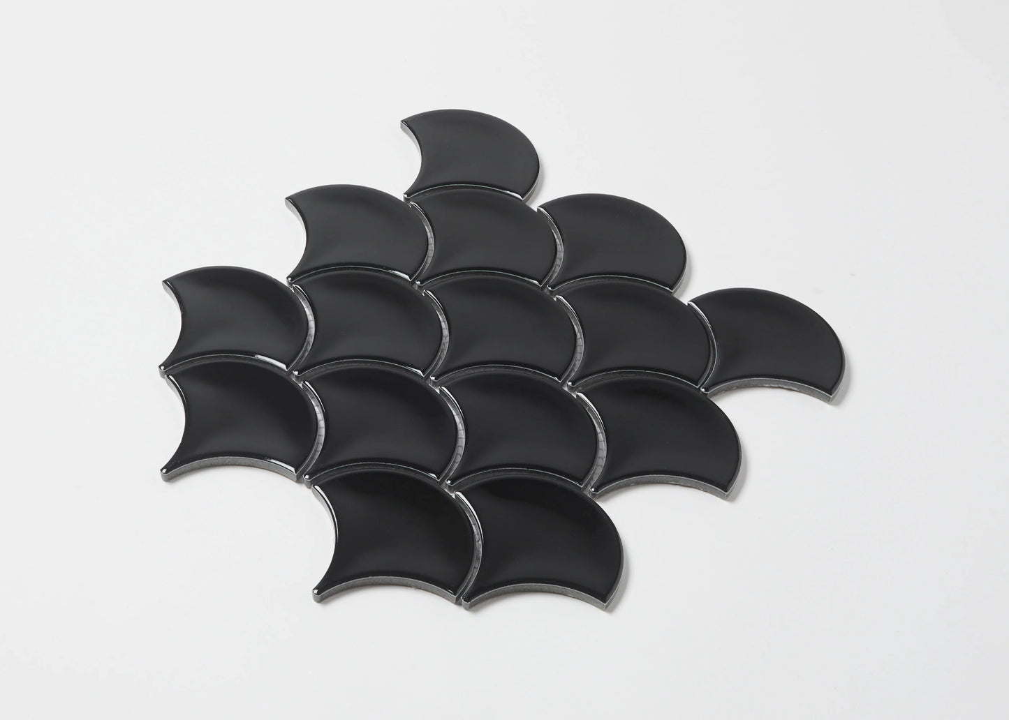 Pack shot of Black Gloss Glazed Porcelain Fishscale 95x87mm tiles arranged in an overlapping scale pattern, showcasing their curved fan shape and glossy black finish.