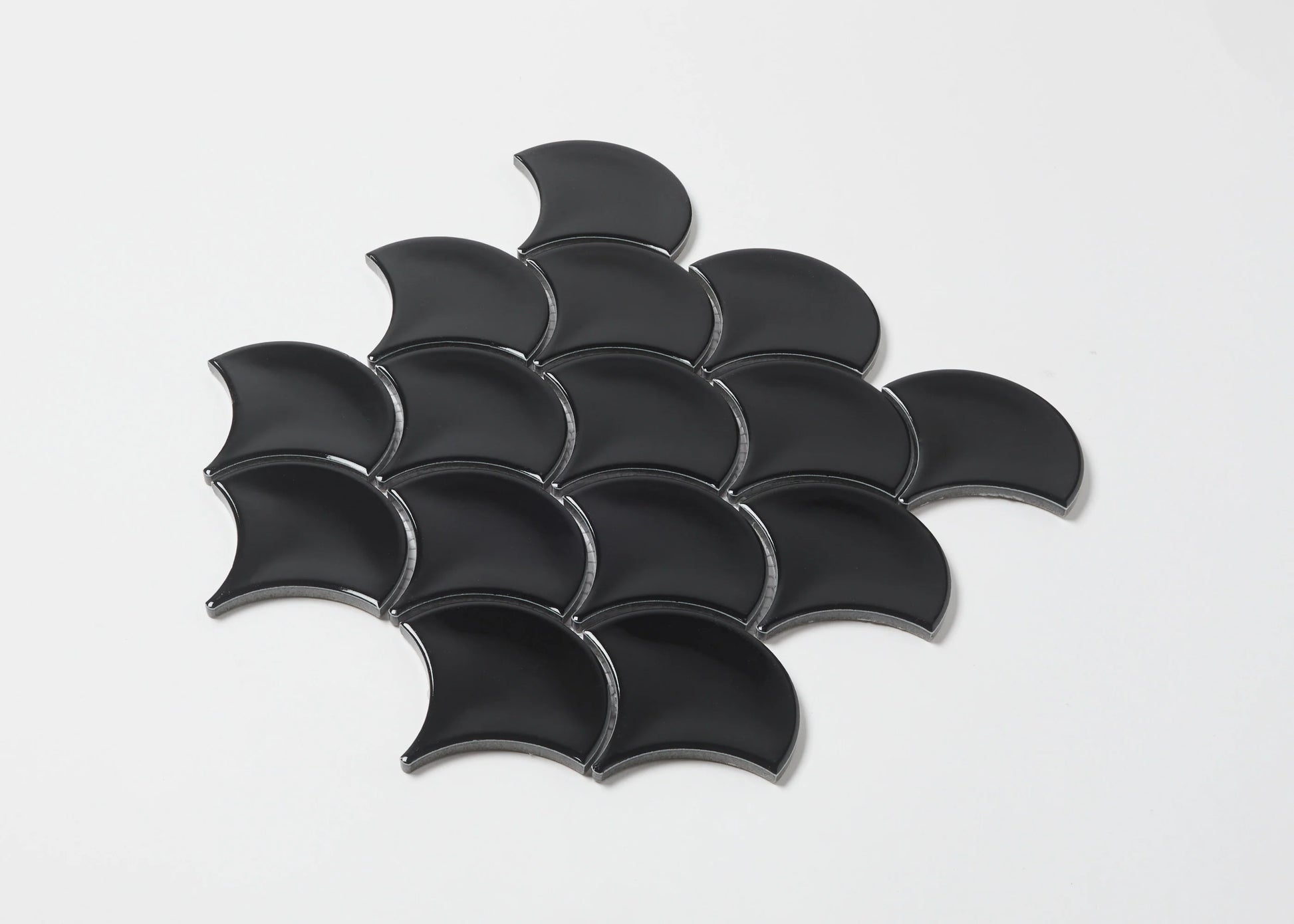 Pack shot of Black Gloss Glazed Porcelain Fishscale 95x87mm tiles arranged in an overlapping scale pattern, showcasing their curved fan shape and glossy black finish.