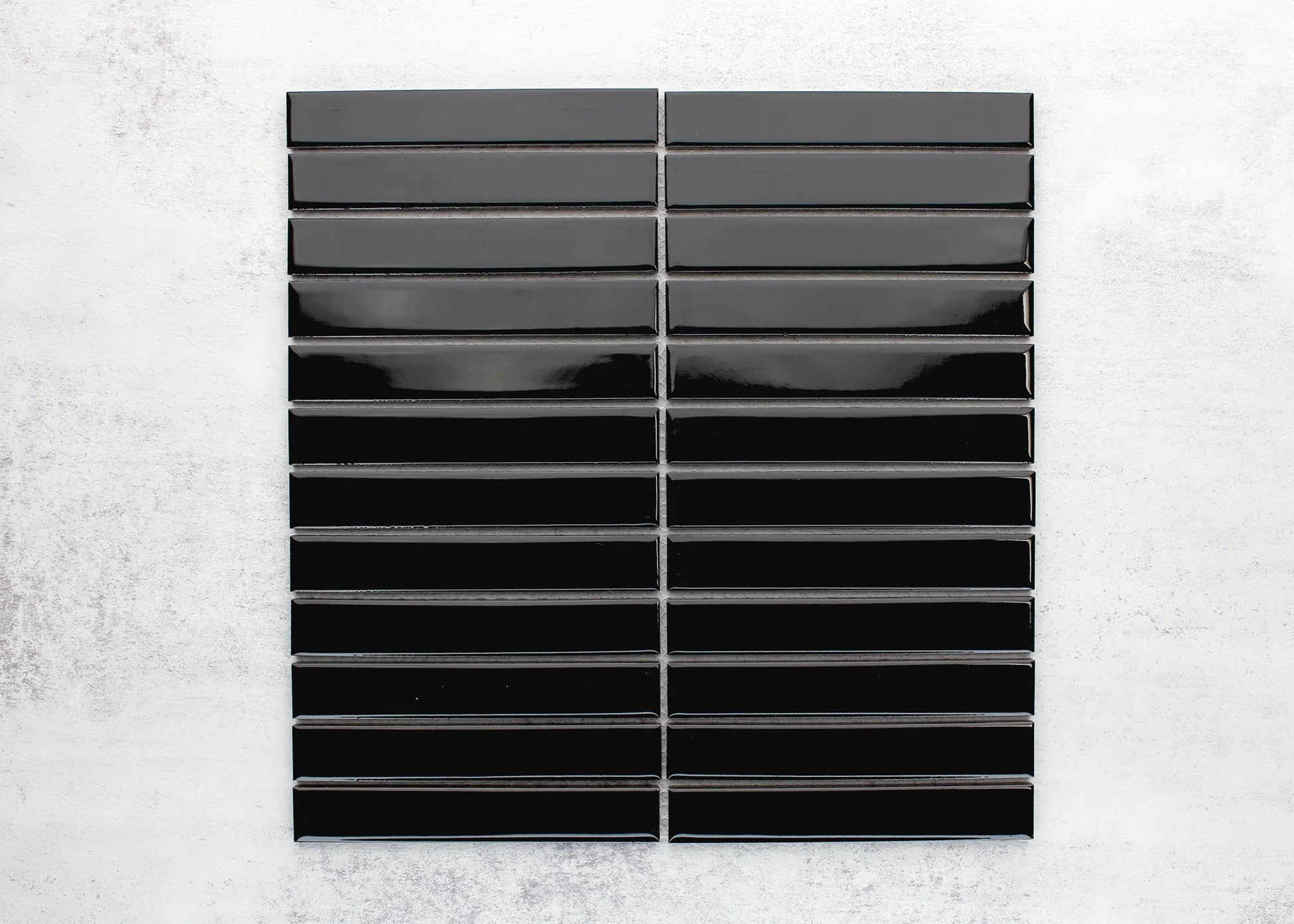 Flat lay pack shot of Black Gloss KitKat Straight Bone Pattern 22x145mm tiles arranged in two stacked columns showing their glossy finish and elongated rectangular shape.