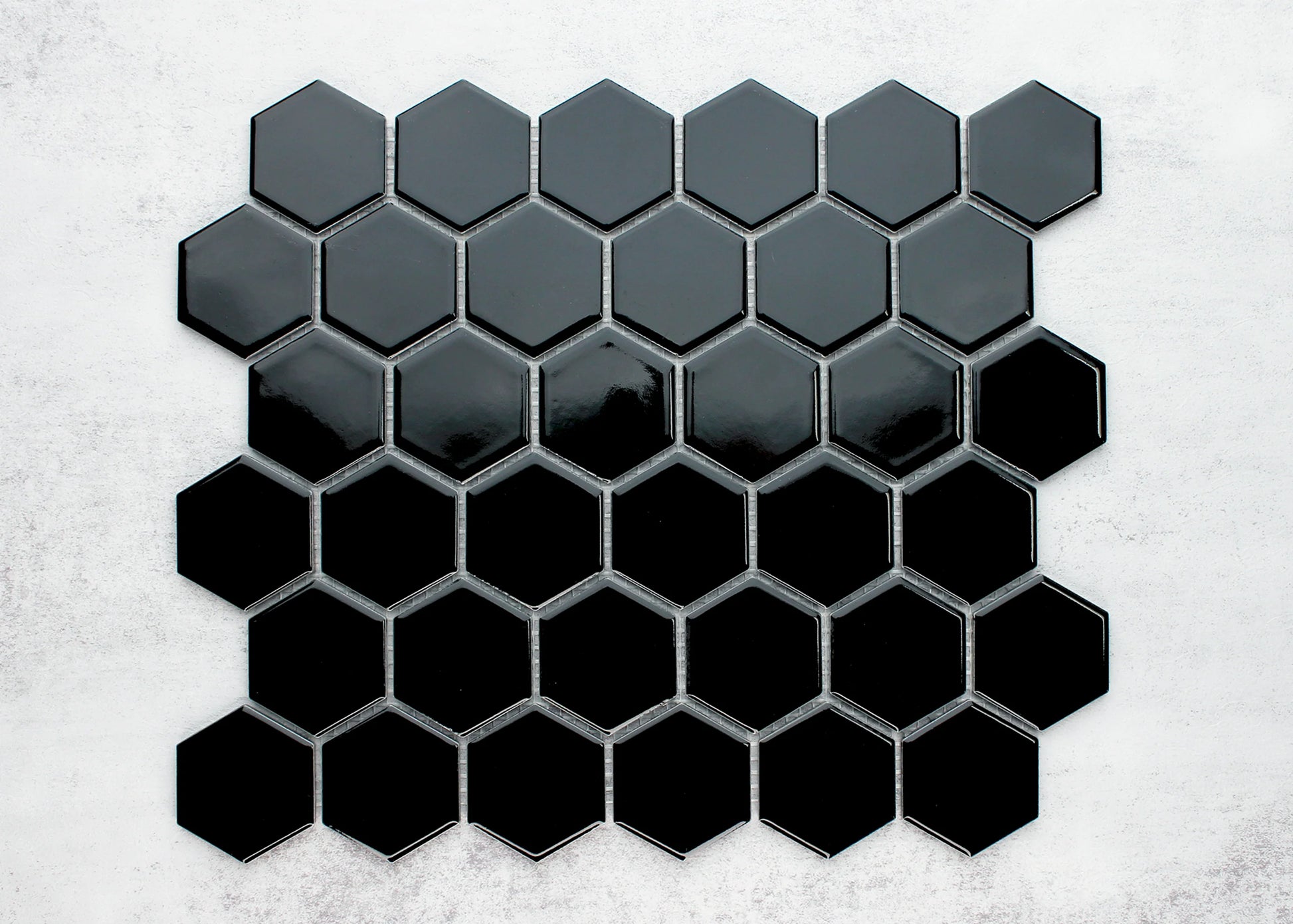 Black Gloss Porcelain Glazed Hexagon 51x59mm tiles arranged in a gradient pattern from dark charcoal to deep gloss black on a light concrete background.