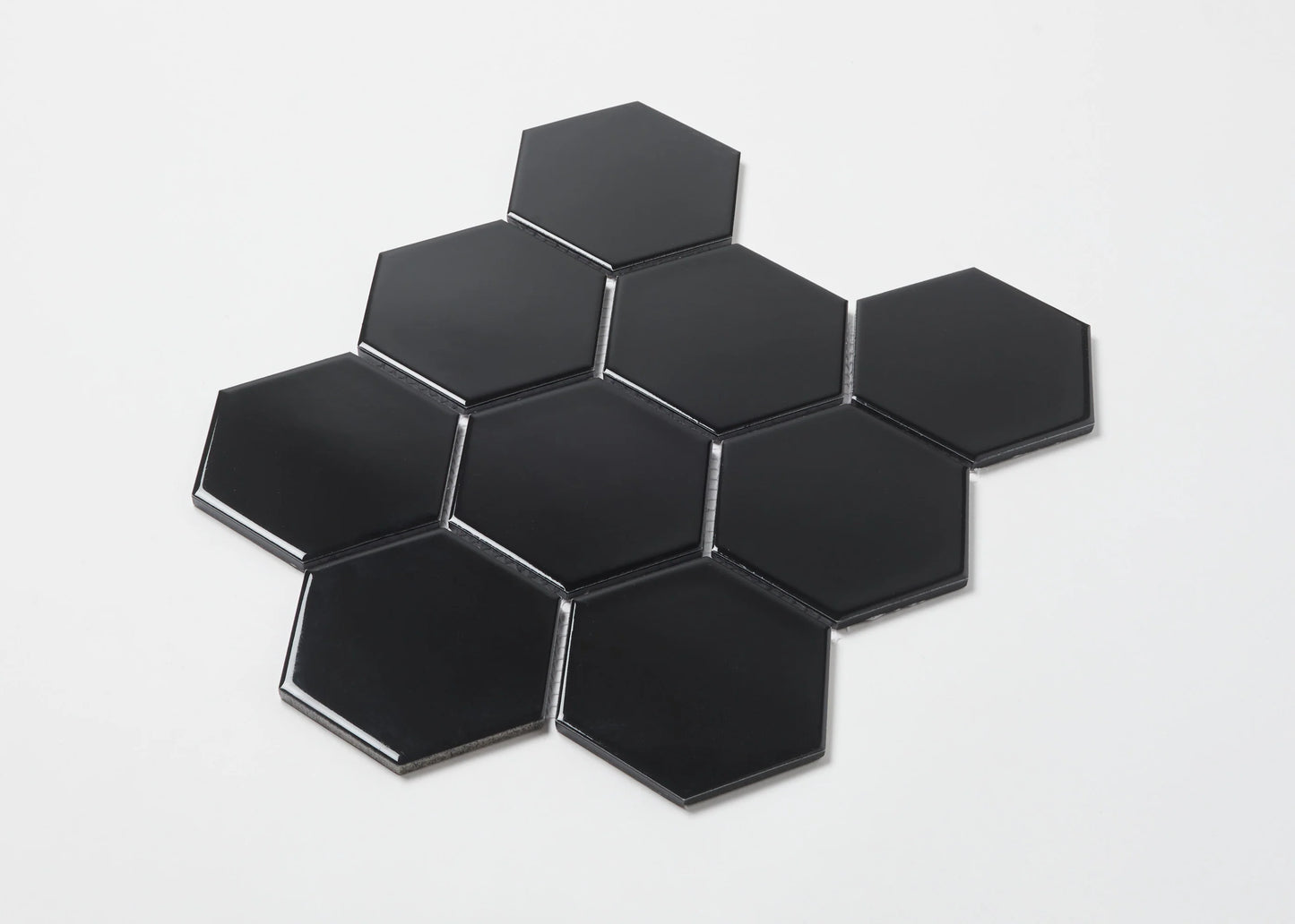 Pack shot of Black Gloss Porcelain Glazed Hexagon 95x110mm tiles arranged in a honeycomb cluster showing glossy black finish and bevelled edges.