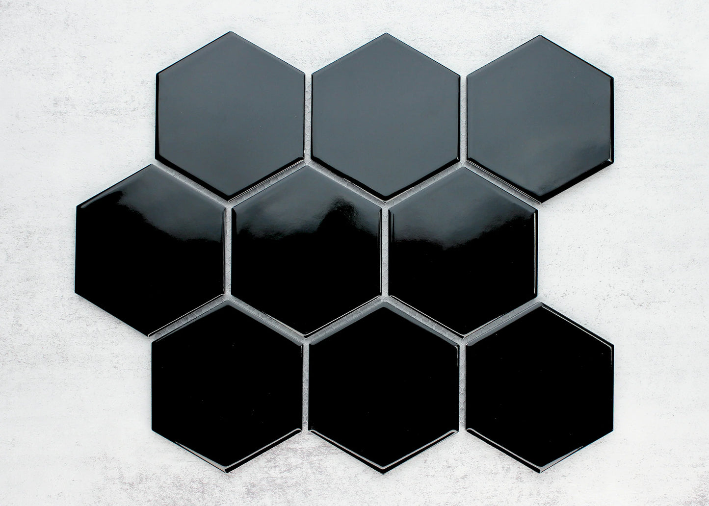 Pack shot of Black Gloss Porcelain Glazed Hexagon 95x110mm tiles arranged in a honeycomb cluster, showing a high-gloss reflective finish in deep black against a light concrete background.
