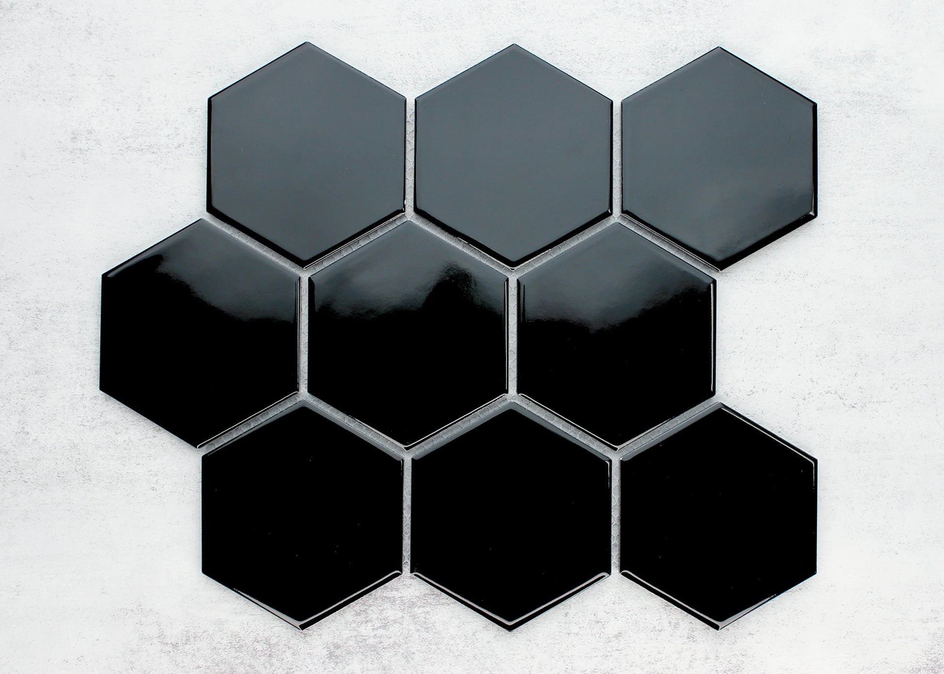 Pack shot of Black Gloss Porcelain Glazed Hexagon 95x110mm tiles arranged in a honeycomb cluster, showing a high-gloss reflective finish in deep black against a light concrete background.