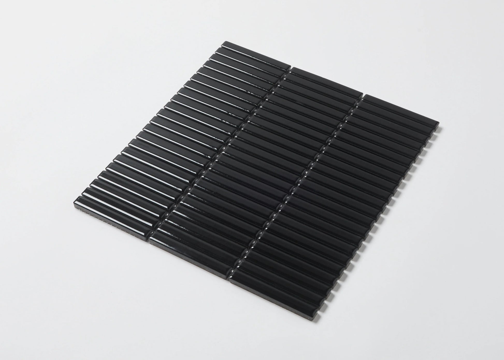 Pack shot of Black Gloss Porcelain Glazed KitKat 12x92mm tiles arranged in a flat lay showing glossy black finger-shaped mosaic strips on mesh backing.