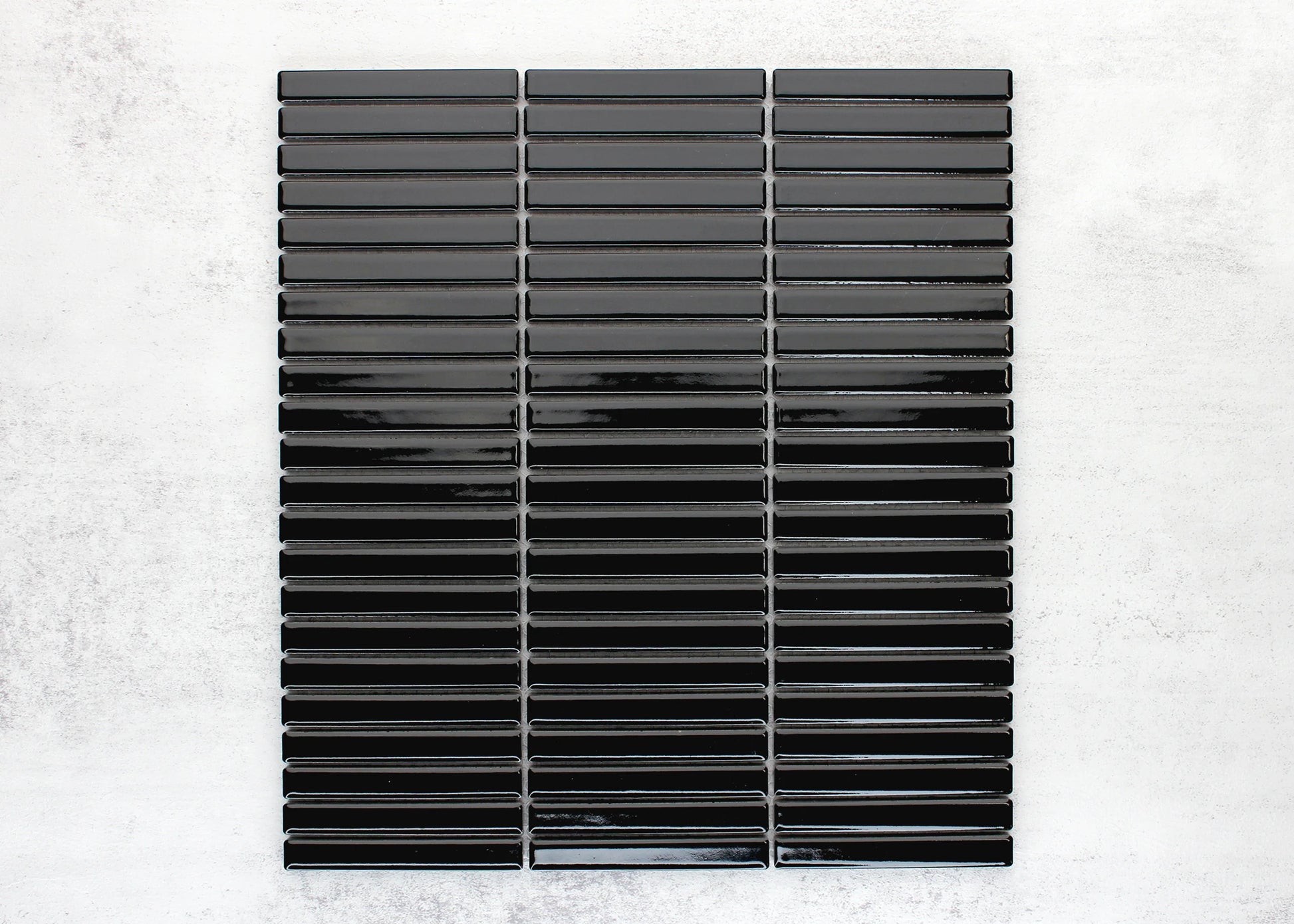 Black Gloss Porcelain Glazed KitKat 12x92mm mosaic sheet displaying glossy elongated finger tiles arranged in three vertical columns on a light concrete background.