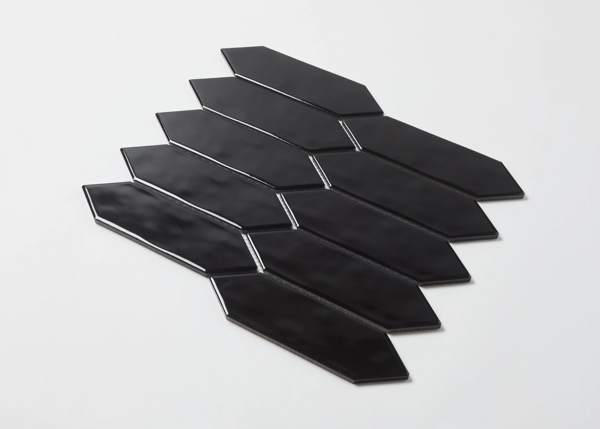Pack shot of Black Gloss Porcelain Glazed Ripple Surface Arrow 55x195mm tiles arranged in a staggered diagonal fan pattern showing glossy black elongated arrow shapes.
