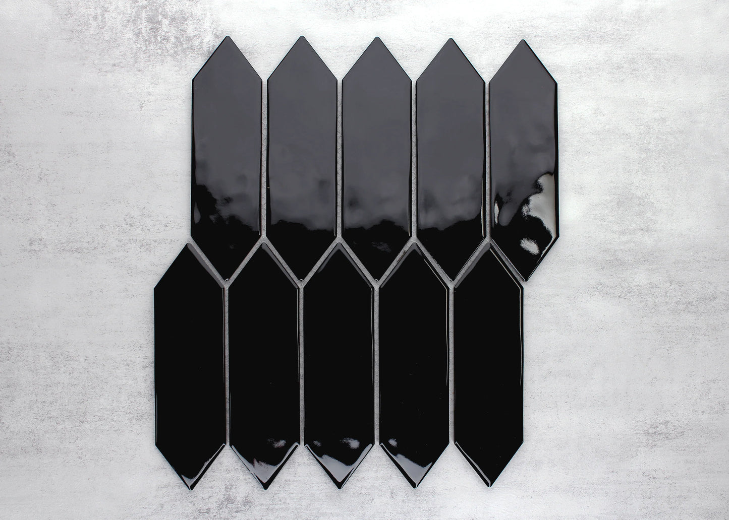 Pack shot of Black Gloss Porcelain Glazed Ripple Surface Arrow 55x195mm tiles arranged in an offset pattern showing glossy black finish and pointed arrow shape.