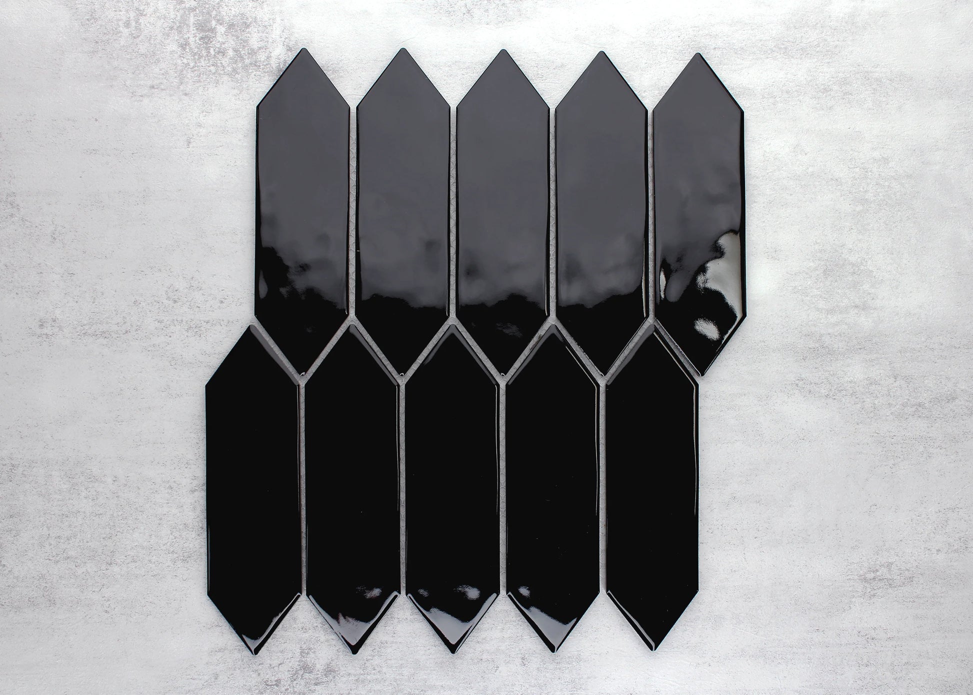 Pack shot of Black Gloss Porcelain Glazed Ripple Surface Arrow 55x195mm tiles arranged in an offset pattern showing glossy black finish and pointed arrow shape.