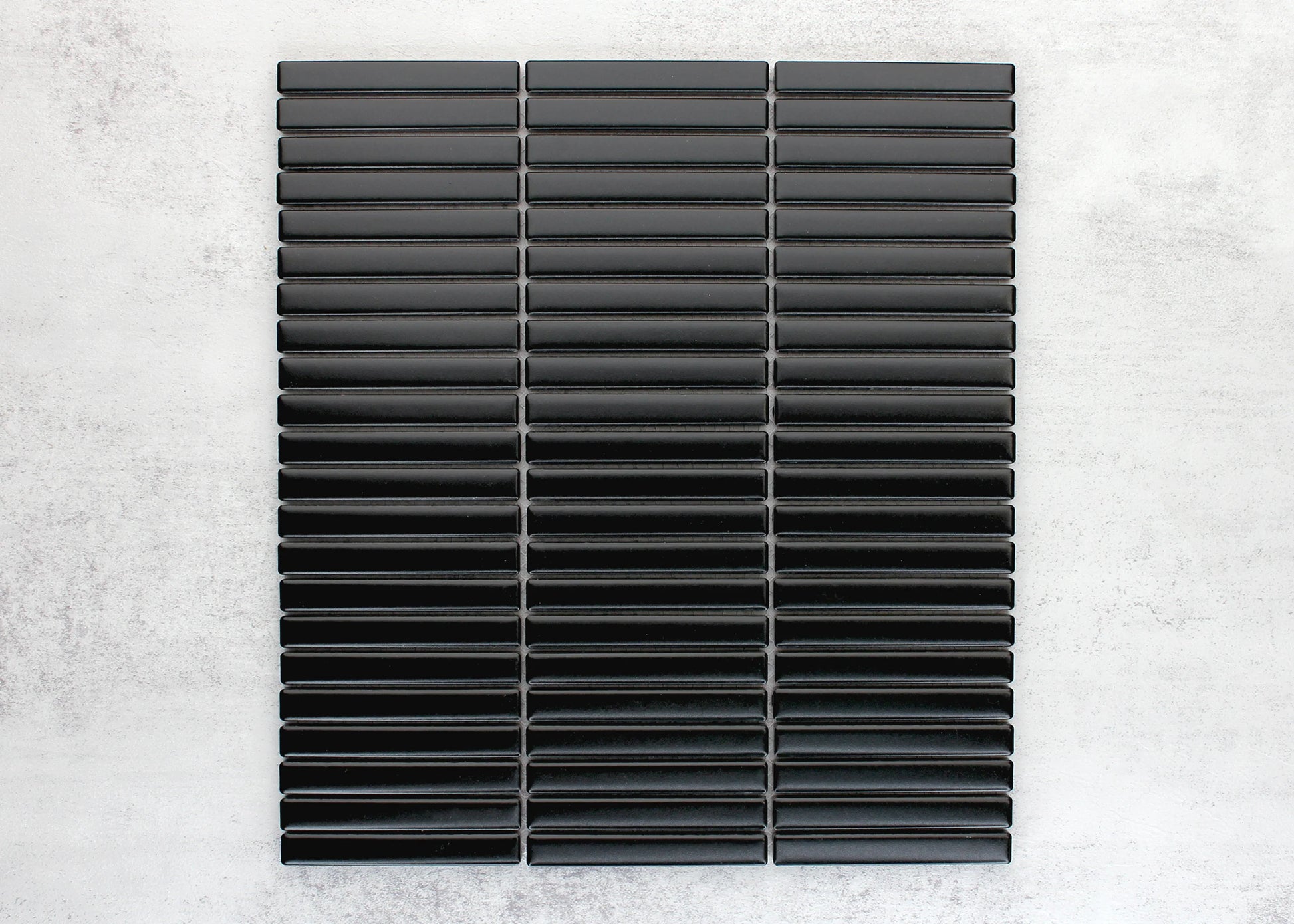 A flat-lay pack shot of the Black Matt Kitkat Straight Bone Pattern 12X92mm tiles arranged in three columns of glossy black elongated ceramic strips.