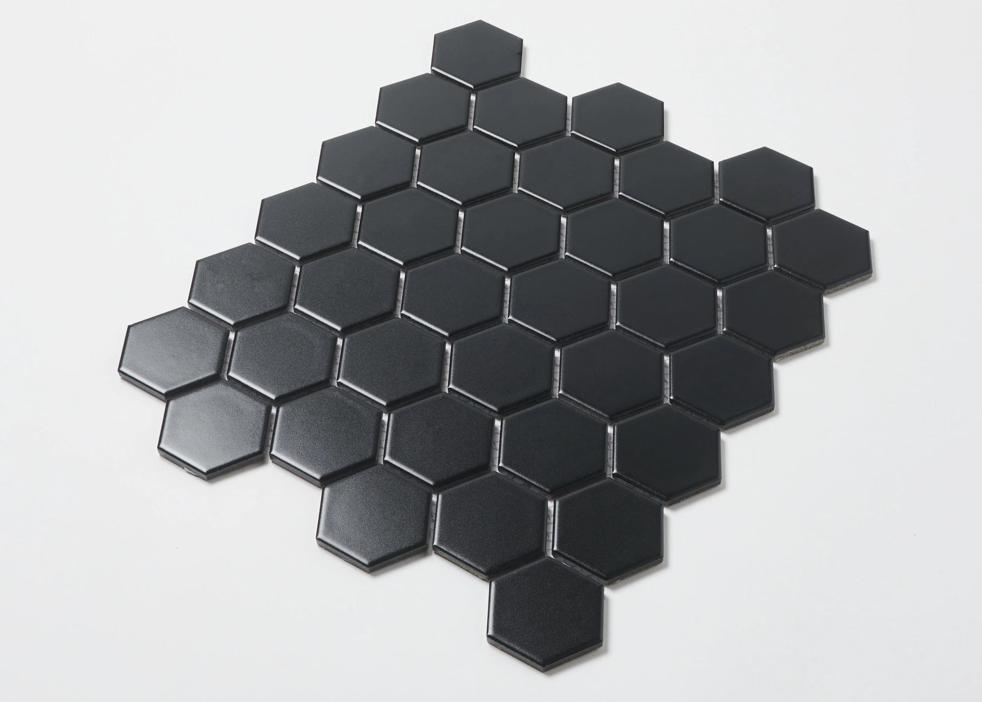 Pack shot of Black Matte Porcelain Glazed Hexagon 51x59mm tiles arranged in a diamond cluster pattern, showcasing the flat matte black finish and geometric hexagonal shape.