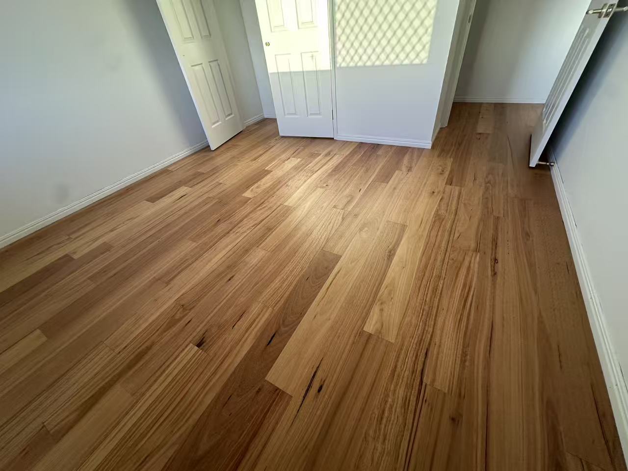 Blackbutt Engineered Australian Classic Flooring 14/3mm installed in an empty bedroom with warm honey tones, white skirting boards, and double doors opening to natural light.