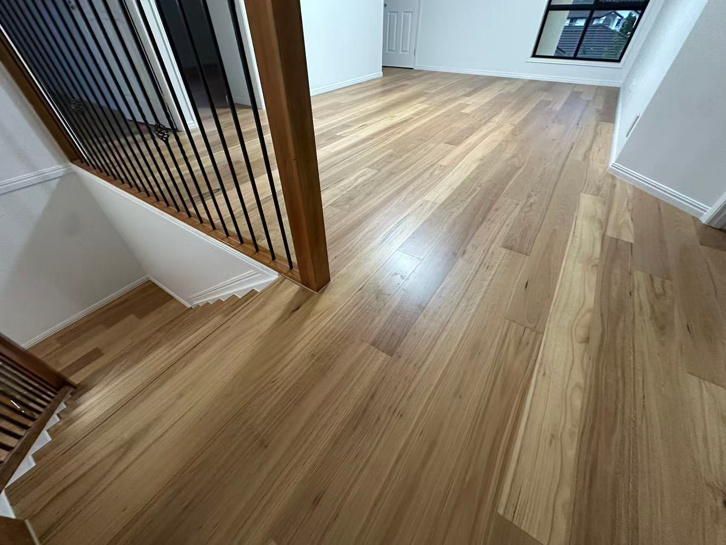 Blackbutt Engineered Australian Classic Flooring 14/3mm installed on an upper-floor hallway and landing area, showcasing warm honey tones, natural timber grain, and a satin finish beside a timber-framed staircase balustrade with black metal spindles.