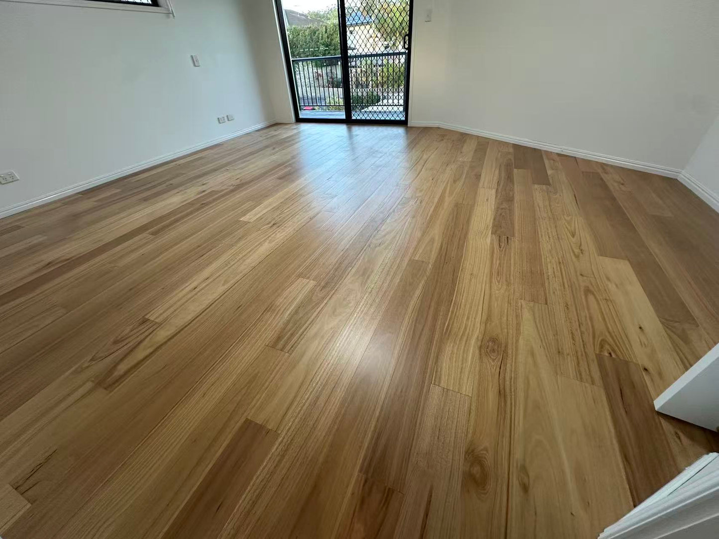 Blackbutt Engineered Australian Classic Flooring 14/3mm installed in an empty sunlit living room with warm natural timber tones, satin finish, and sliding balcony door.