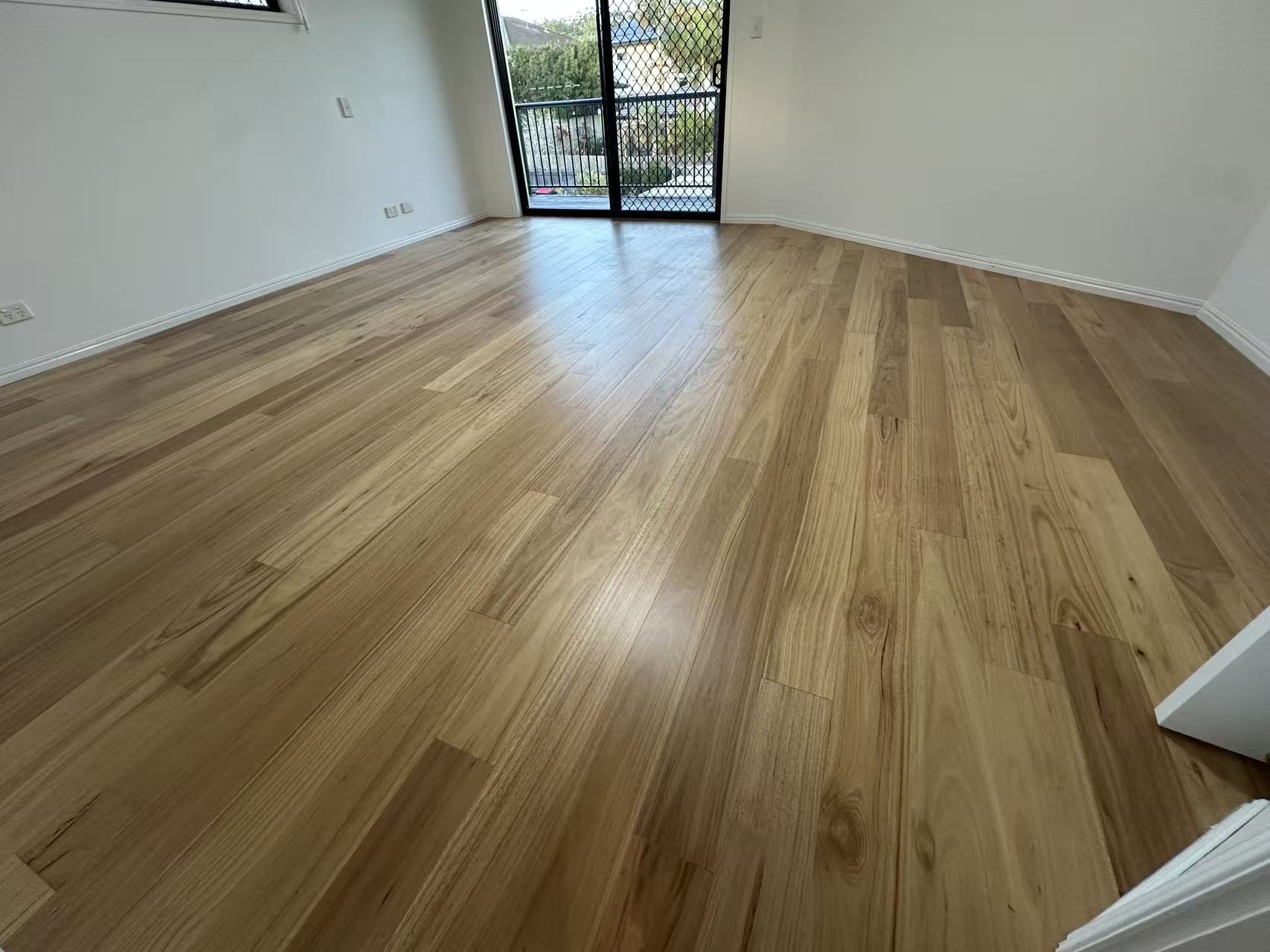 Blackbutt Engineered Australian Classic Flooring 14/3mm installed in an empty sunlit living room with warm natural timber tones, satin finish, and sliding balcony door.