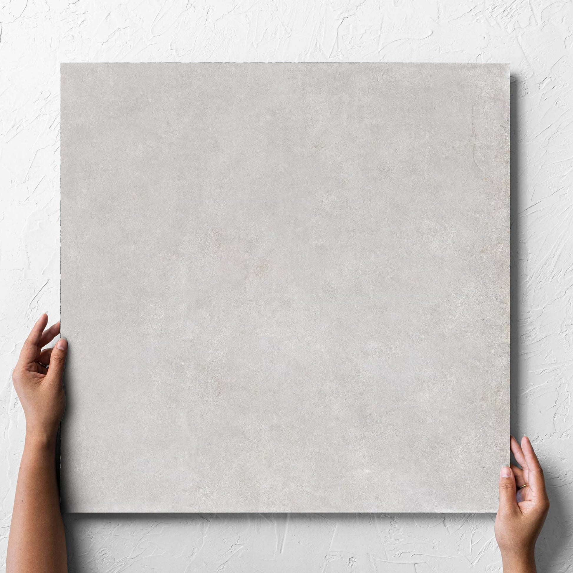 Hand holding a single Boston Silver Matt 600x600mm tile against a white rendered wall, showing the tile surface