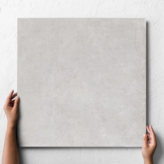 Hand holding a single Boston Silver Matt 600x600mm tile against a white rendered wall, showing the tile surface
