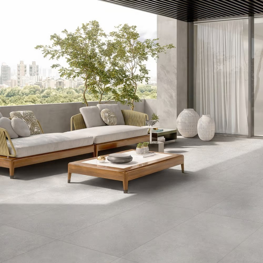 Boston Silver Matt Rectified 300x600mm tiles covering a contemporary outdoor terrace lounge with timber sofa, coffee table, and city skyline views.