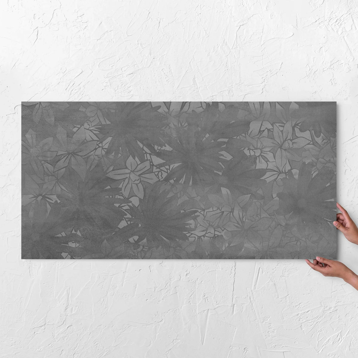 Hands holding a Botanica Lotus Decor 600x1200mm tile against a white rendered wall, showing the matt surface