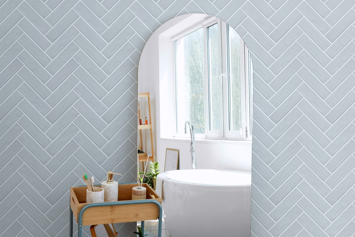 Brava Rustic Blue Gloss 60x217mm tiles installed in a herringbone pattern on a bathroom wall, complementing a freestanding white bathtub and bamboo vanity trolley.