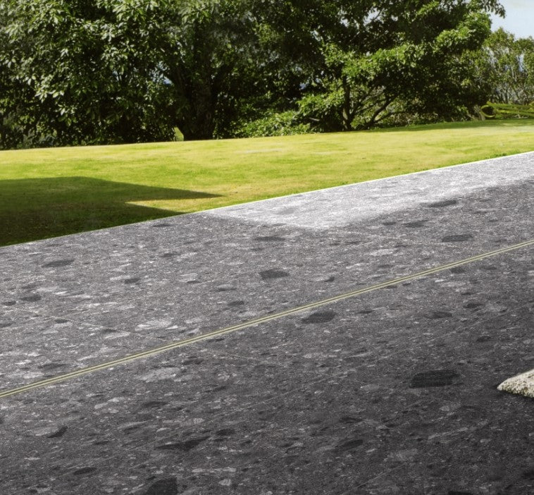 Breccia Dark Grey 600x600mm tiles laid as an outdoor driveway surface beside a lush green lawn with mature trees in the background.