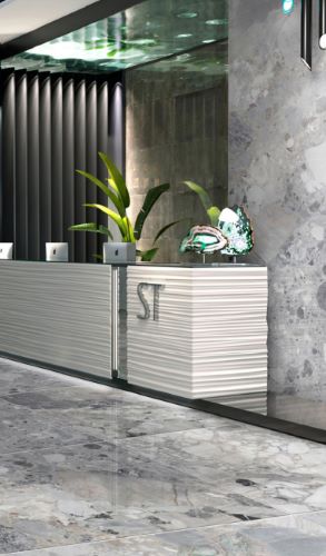 Breccia Light Grey 600x600mm porcelain tiles installed on the floor of a contemporary hotel lobby featuring a sculptural white reception desk and marble-effect walls.