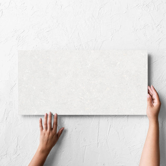 Hand holding a single Brighton Bianco Matt 300x600mm tile against a white rendered wall, showing the matt surface