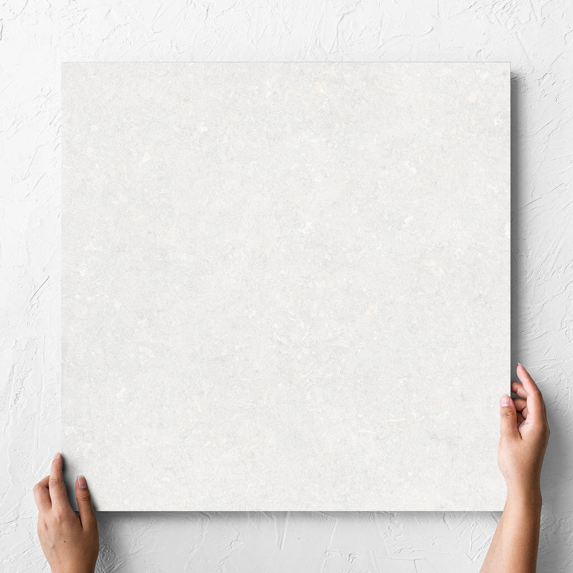Hand holding a single Brighton Bianco Matt 600x600mm tile against a white rendered wall, showing the matt surface