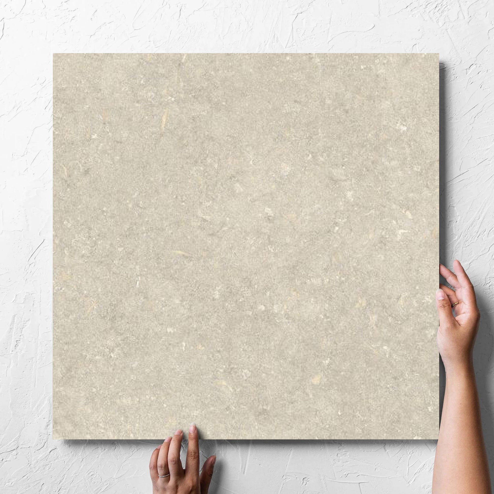 Hand holding a single Brighton Earth Matt 600x600mm tile against a white rendered wall, showing the matt surface