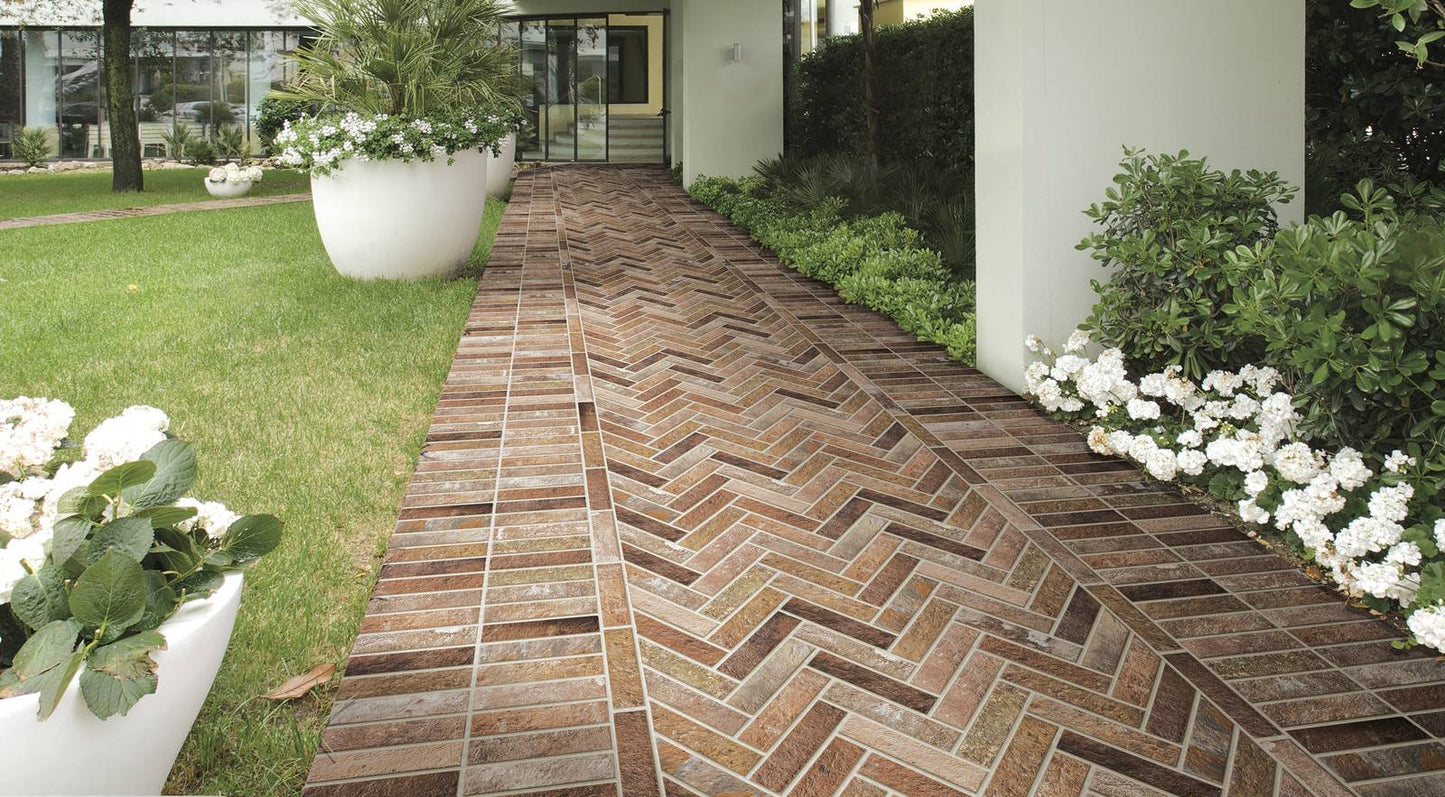 Bristol Red Brick Tile 60x250mm laid in a herringbone pattern along an elegant outdoor garden pathway bordered by white flowering shrubs and lush green lawn.