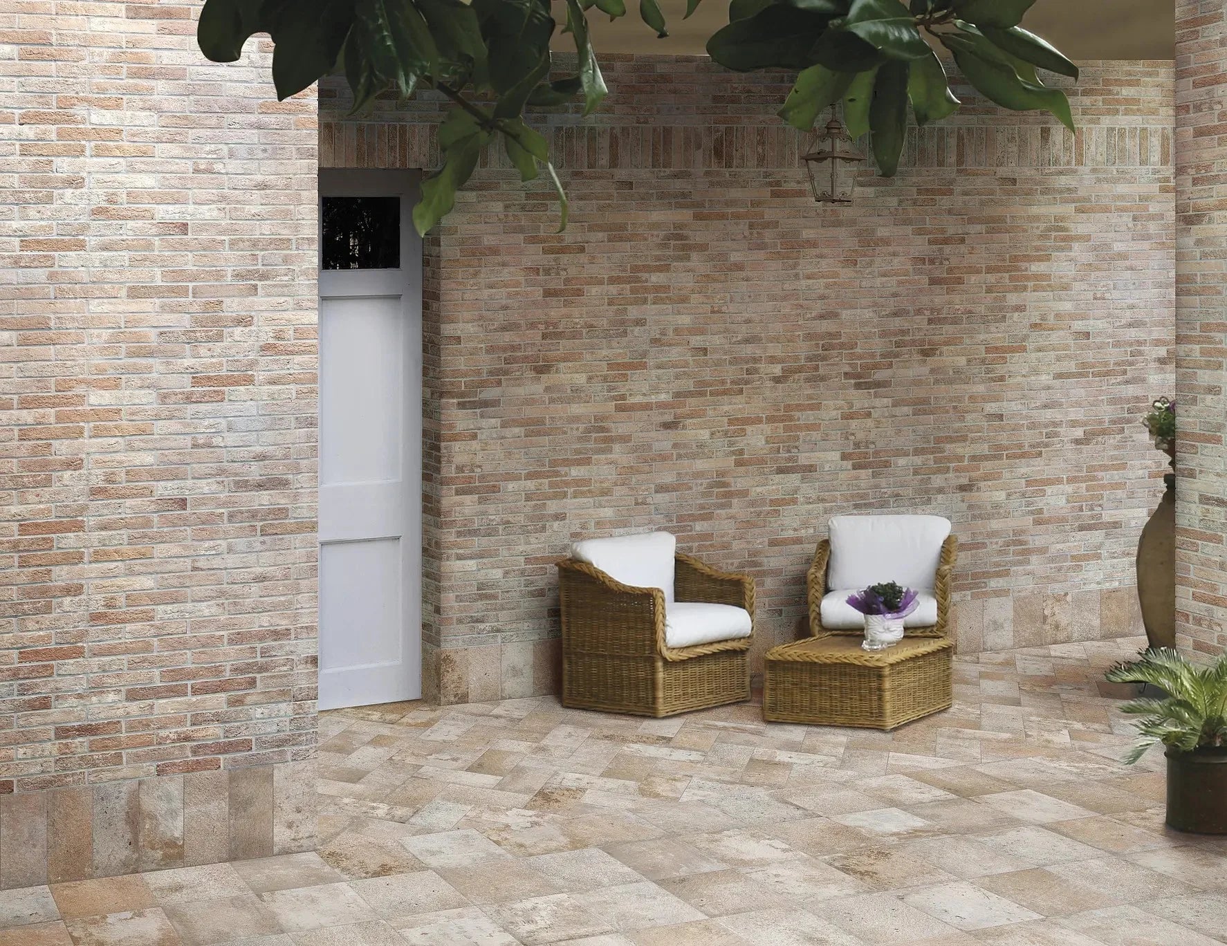 Bristol Rust Brick Tile 60x250mm covering a warm-toned outdoor patio wall alongside travertine floor tiles, wicker chairs, and hanging lantern.