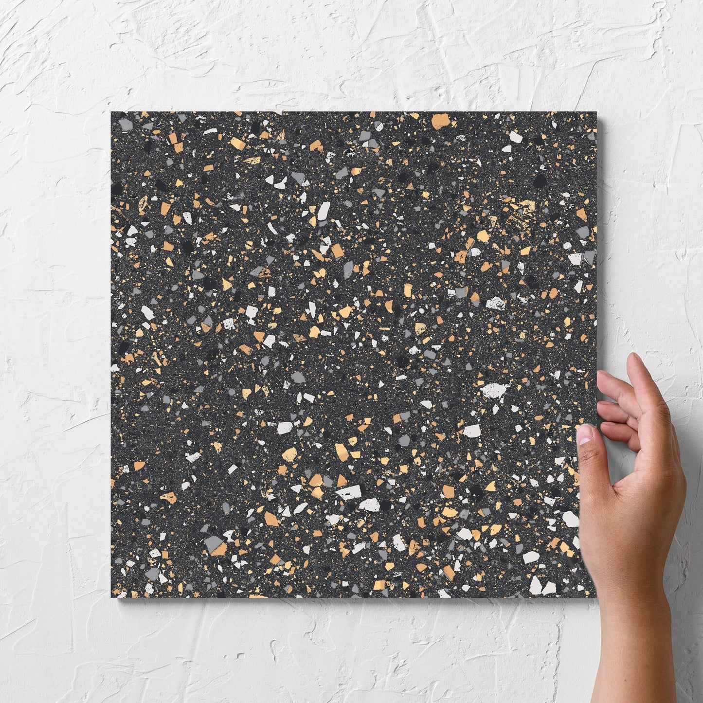 Hand holding a single C Venice 300x300 Matt Graphite Terrazzo Look Rectified tile against a white rendered wall, showing the terrazzo look tiles surface