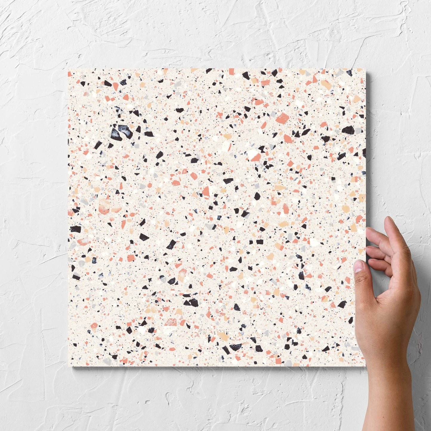 Hand holding a single C Venice 300x300 Matt Pink Terrazzo Look Rectified tile against a white rendered wall, showing the tile surface