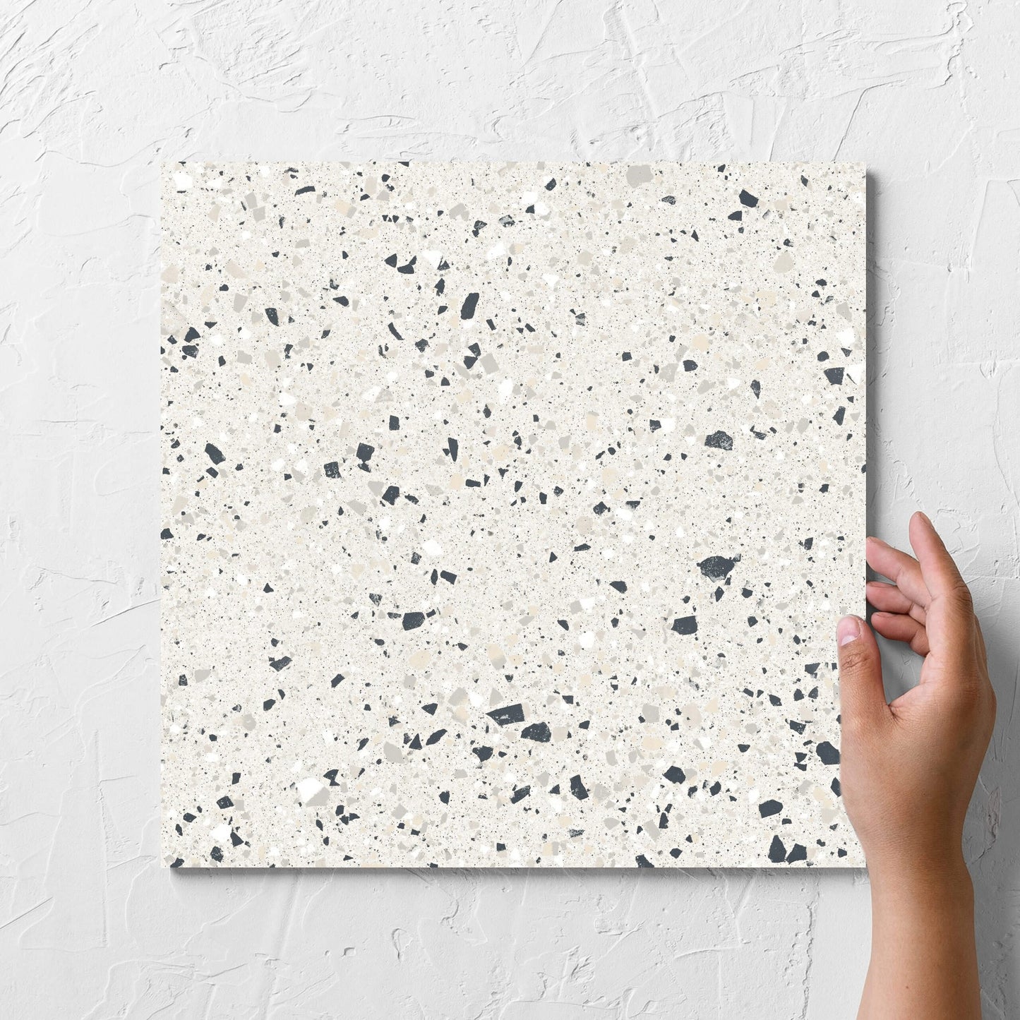Hand holding a single C Venice 300x300 Matt Silver Terrazzo Look Rectified tile against a white rendered wall, showing the tile surface