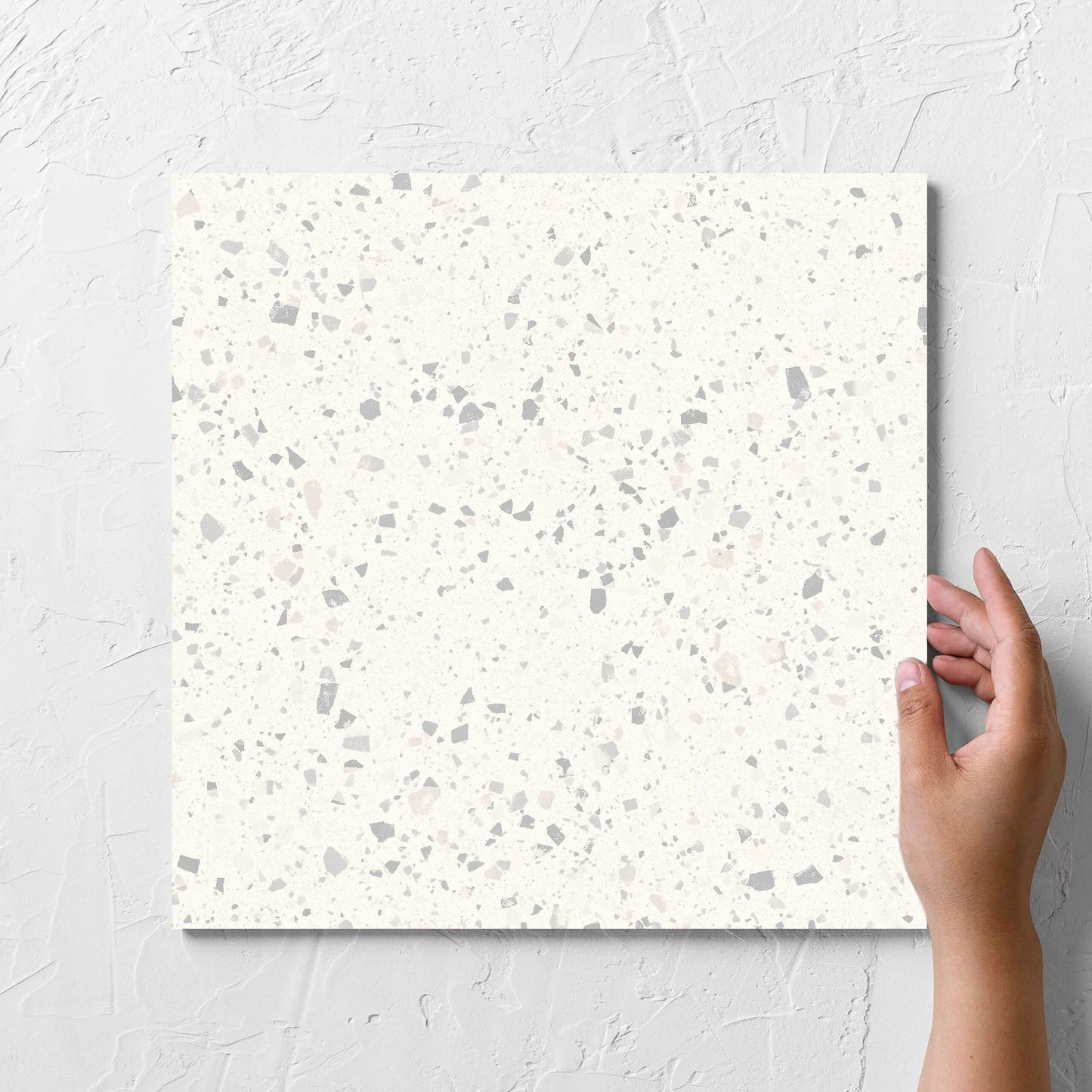 Hand holding a single C Venice 300x300 Matt Zinc Terrazzo Look Rectified tile against a white rendered wall, showing the tile surface