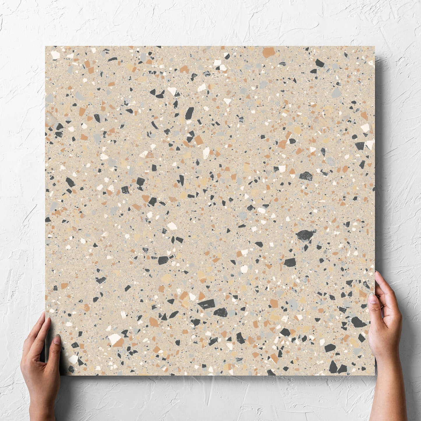 Hand holding a single C Venice 600x600 Matt Beige Terrazzo Look Rectified tile against a white rendered wall, showing the tile surface