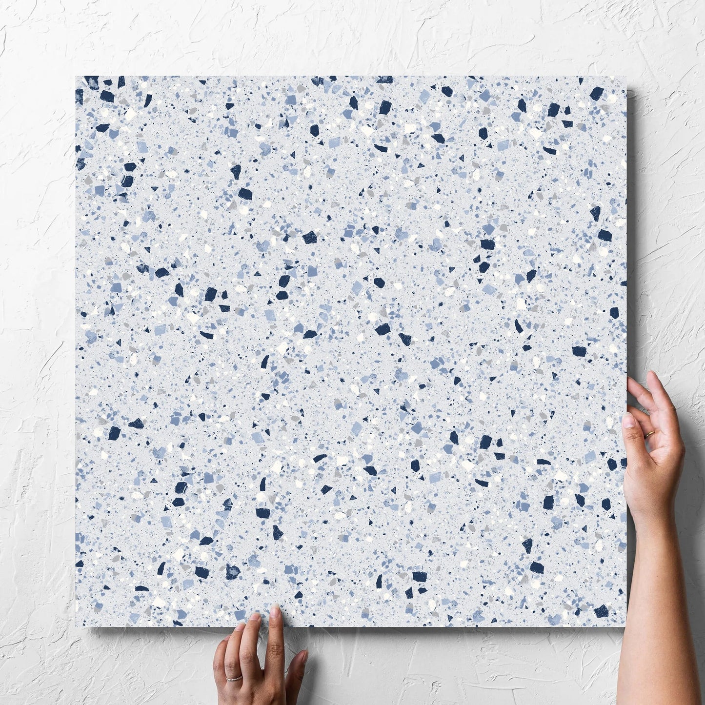 Hand holding a single C Venice 600x600 Matt Blue Terrazzo Look Rectified tile against a white rendered wall, showing the tile surface