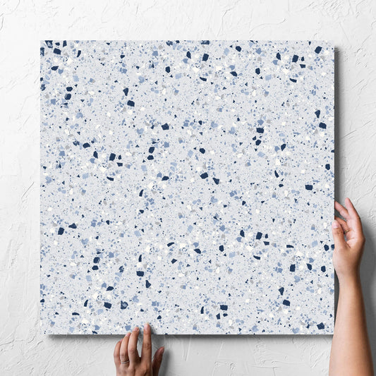 Hand holding a single C Venice 600x600 Matt Blue Terrazzo Look Rectified tile against a white rendered wall, showing the tile surface