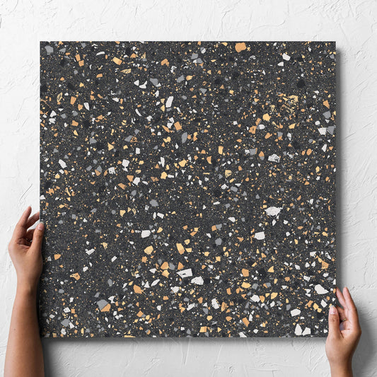 Hand holding a single C Venice 600x600 Matt Graphite Terrazzo Look Rectified tile against a white rendered wall, showing the tile surface