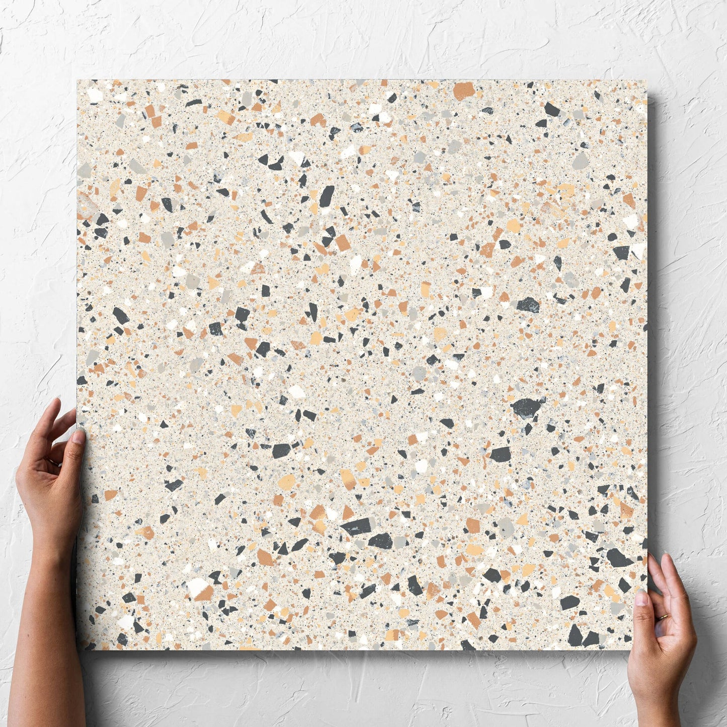 Hand holding a single C Venice 600x600 Matt Ivory Terrazzo Look Rectified tile against a white rendered wall, showing the tile surface