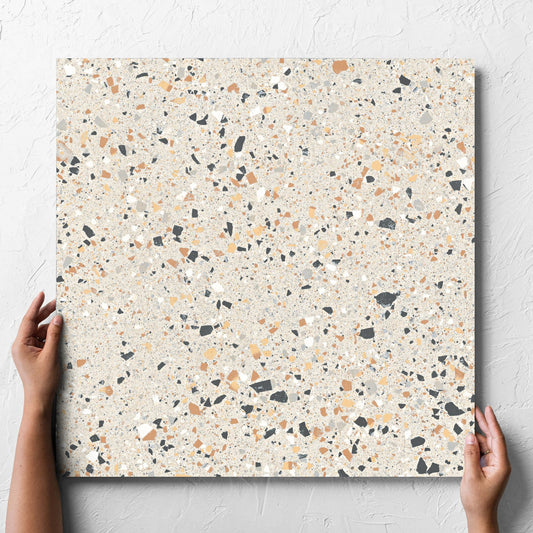 Hand holding a single C Venice 600x600 Matt Ivory Terrazzo Look Rectified tile against a white rendered wall, showing the tile surface
