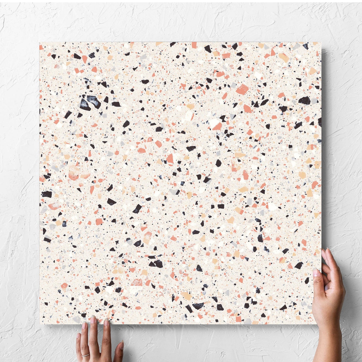 Hand holding a single C Venice 600x600 Matt Pink Terrazzo Look Rectified tile against a white rendered wall, showing the pink matt surface